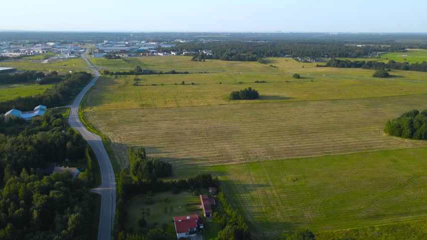 Drone view of a freshly cut farm field with mowing lines rural road house and forest on a sunny summer day.