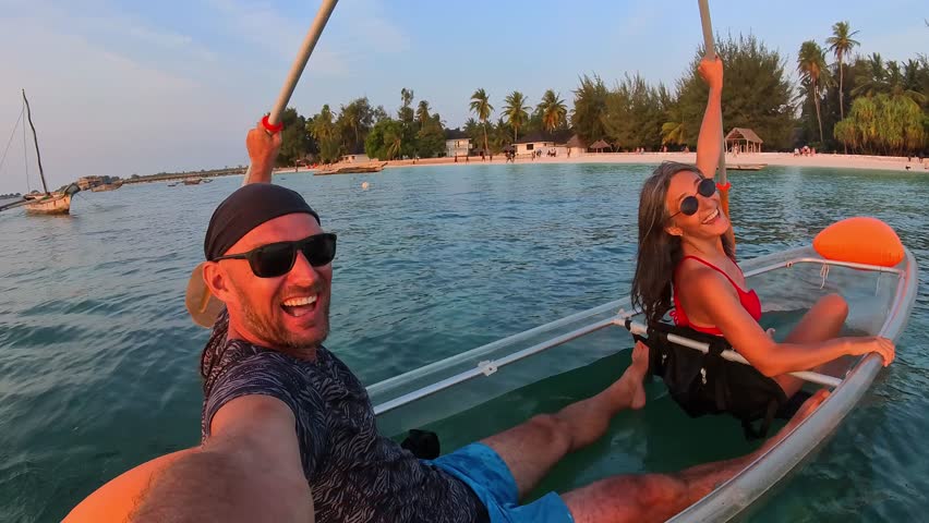 Happy funny cute couple cheers during a sunset clear kayak tour in Zanzibar. Point-of-view selfie capturing authentic joy, adventure, and tropical island vibes. Man woman bonding while travel together