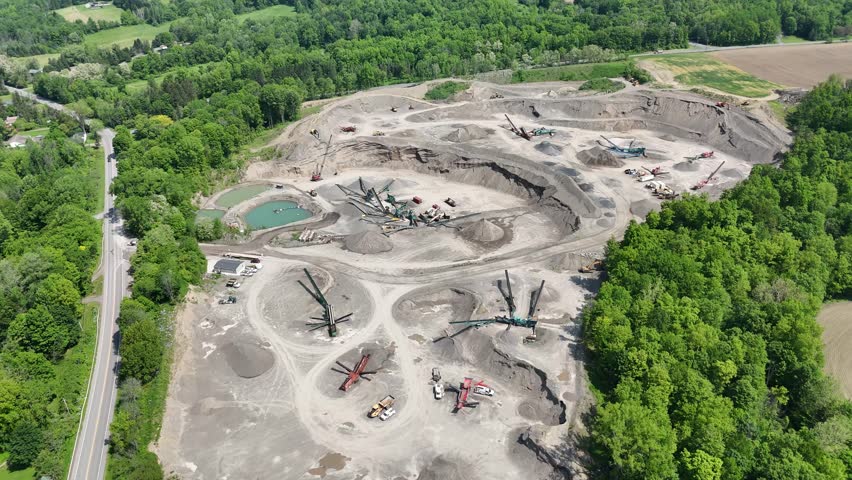 An industrial mining site that is undergoing extraction of raw materials as heavy equipment can be seen scattered throughout the area enclosed by forest and vegetation.