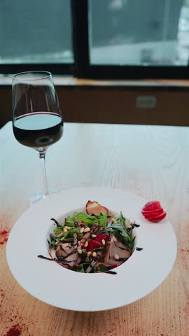 fresh salad with arugula, meat ham and strawberry and glass of red wine on table