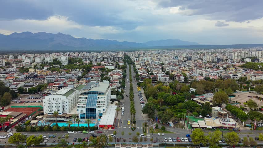 Forward aerial view above a palm lined boulevard and urban district near Konyaaltı Beaches, Antalya, Turkey, with the Taurus Mountains background