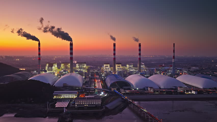 Industrial landscape of a thermal power plant with smoke stacks emitting smoke at sunset