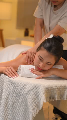 Woman enjoying back massage at spa with therapist in warm calm wellness, Vertical vdo.