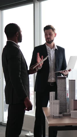 A diverse group of professionals in a modern office setting collaborates around a table displaying architectural models of skyscrapers