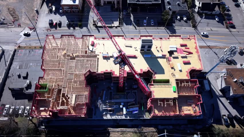 Rising Aerial Shot Of A Crane Above An Apartment Building Being Built By Construction Workers In America.