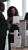 Four professionals examine a detailed scale model of urban skyscrapers during a planning meeting, with laptops and notes in a bright office - Powered by Shutterstock - Get 15% off with code: PIKWIZARD15