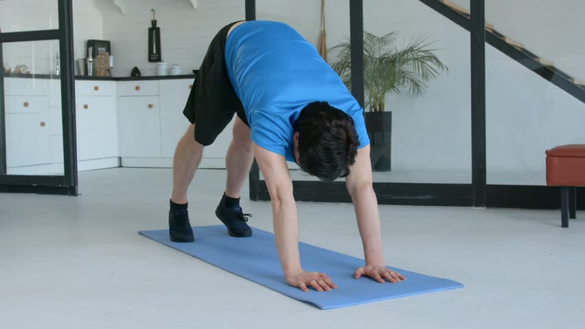 Determined sporty fit man performing pike push up exercise, strengthening shoulder muscles and improving core stability while working out in domestic room.