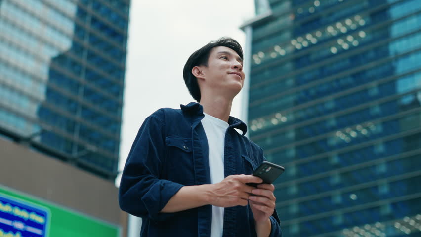 Portrait of young Asian man standing outdoor happy smiling use mobilephone.Handsome young asian man dressed casually walking spending time outdoors at city urban,carrying backpack,using mobile phone
