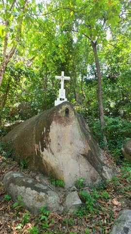 A vertical video of the Stations of the Cross Station 2 set along a serene tropical hillside, featuring a white cross monument surrounded by lush greenery. This video captures a quiet and contemplative atmosphere ideal for themes of faith, reflection, sacrifice, and spirituality. Suitable for Christian content, church presentations, Good Friday observances, Easter storytelling, and meditative visual projects.