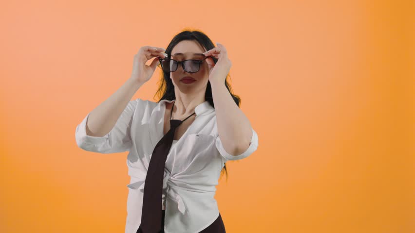 Young woman trying on sunglasses on orange background