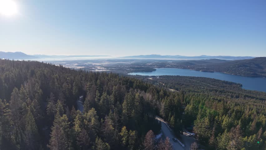 Aerial shot of forested hillsides and distant lakes under a clear blue sky near Whitefish, Montana.
