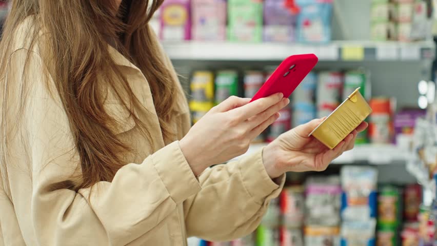 Woman scanning product with smartphone in store, checking information such as price, reviews and details before purchase, smart shopping behavior in supermarket or pet shop