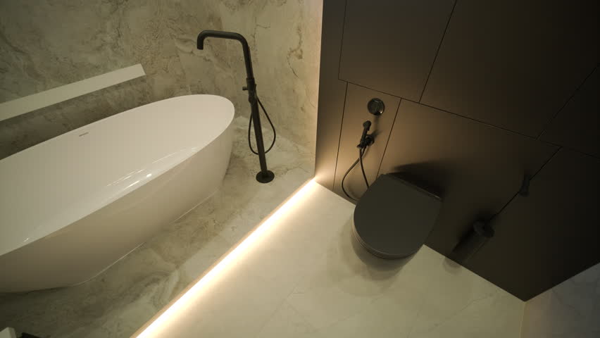 Luxury modern bathroom interior featuring a white freestanding bathtub and a unique stone vessel sink. The room is decorated with marble tiles, a large oval backlit mirror, and black matte fixtures in a minimalist contemporary style.