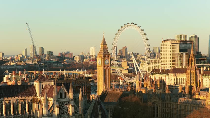 Warm sunrise over London illuminating iconic Big Ben, Westminster Abbey, and Millennium Wheel on a tranquil morning with a clear sky above the city