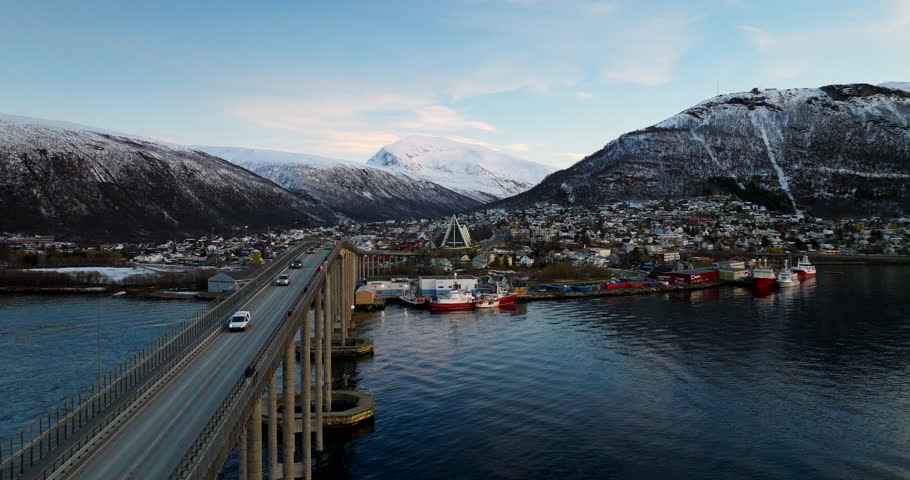 Tromsø bridge, harbor, and Arctic Cathedral with snow-covered mountains in early winter, Norway. Aerial forward, copy space