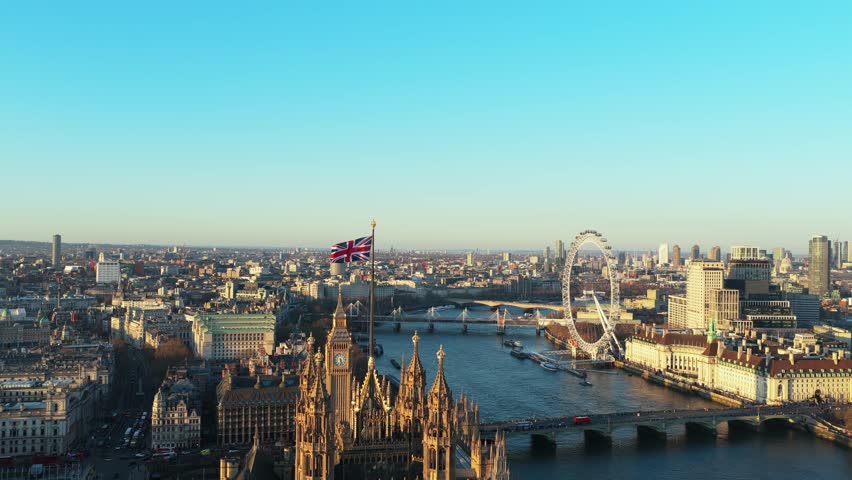 Waving Union Jack flag over Palace of Westminster showcasing Big Ben, River Thames, London Eye, and Westminster Bridge in London, United Kingdom