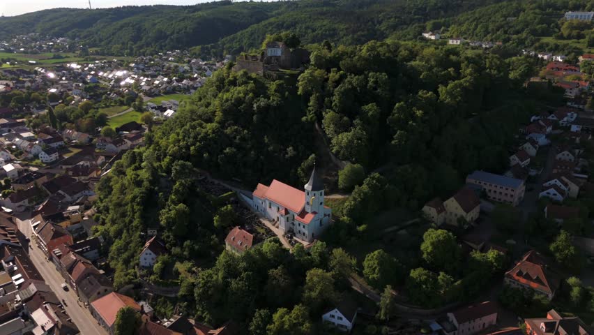 Die Pfarrkirche St. Michael mit achteckigem Turm und Zeltdach liegt in Donaustauf, Landkreis Regensburg, nahe dem Aschenbuegel und den Ruinen der Burg Donaustauf. Eindrucksvolle Luftansicht. 
