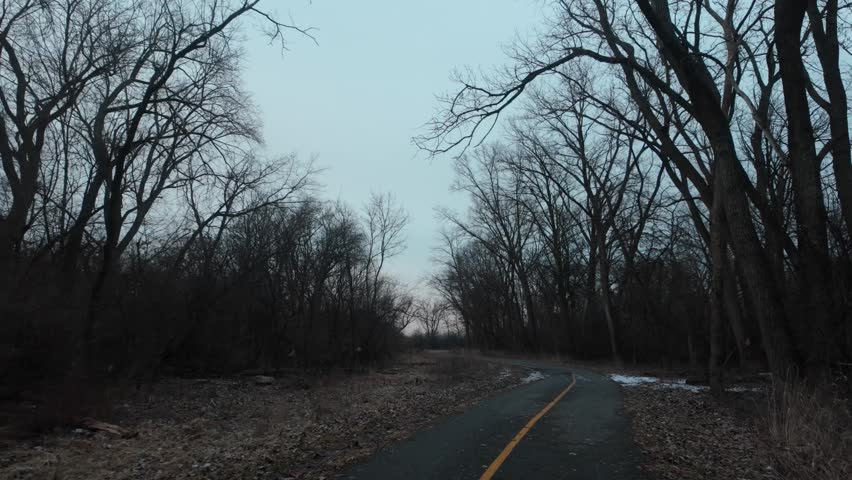 Walking down a forest preserve bike trail in winter. Trees have no leaves and snow piles are on the ground.