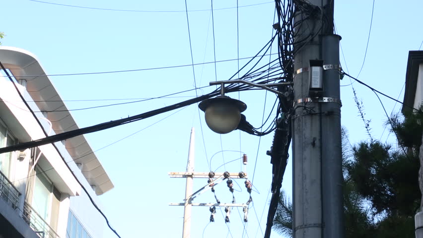 scenic view of a utility pole with tangled power lines and a street lamp in an alley of south korea