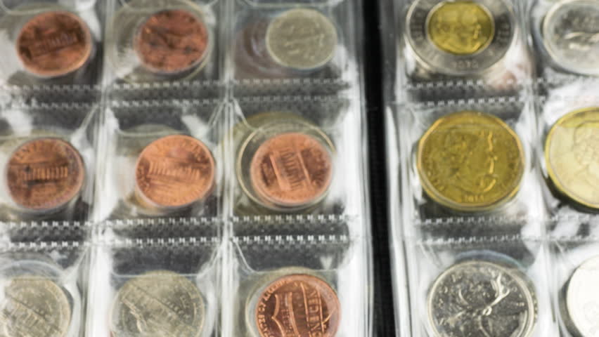 A numismatist in white cotton gloves carefully holds a US quarter dollar while examining a coin collection album. This close-up shot highlights the detailed portrait of George Washington on the silver coin against a background of various currency. The professional handling and organized display showcase the value and preservation of a diverse numismatic hobby.