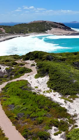 Vertical aerial drone shot of a breathtaking coastline in Cape Le Grand National Park, Western Australia. Turquoise ocean waters, pristine sandy beach, and warm golden hour light.