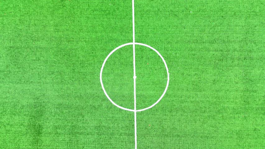 High angle drone shot of a person dribbling a ball around the center circle of a green artificial turf field in Evrenye, Inebolu, Kastamonu, Turkey.