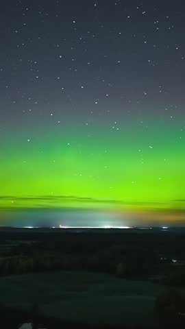 Green aurora borealis glowing above dark forest horizon under starry night sky