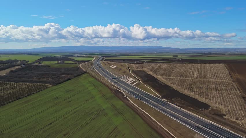 Szikszó, Hungary’s M30 motorway and interchange traverse green fields and rolling hills in Borsod-Abaúj-Zemplén County, viewed from an elevated aerial perspective on a clear daytime.
