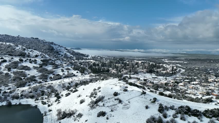 Aerial view of Merom Golan and Bental Reservoir covered in snow with wind turbines rising above the fog, Golan Heights, Israel