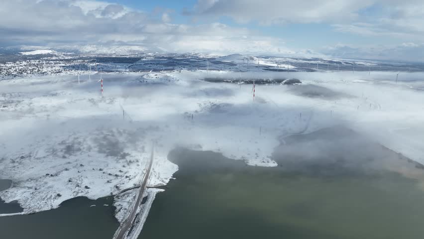 Aerial view of Merom Golan and Bental Reservoir covered in snow with wind turbines rising above the fog, Golan Heights, Israel
