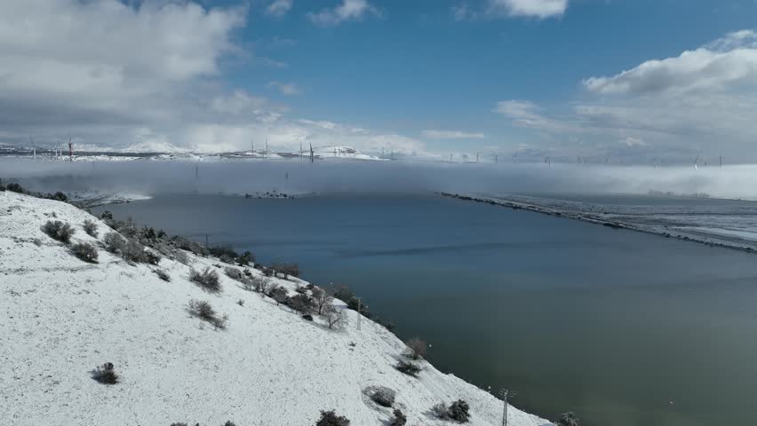 Aerial view of Merom Golan and Bental Reservoir covered in snow with wind turbines rising above the fog, Golan Heights, Israel