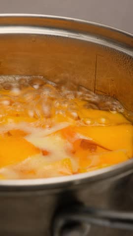 Orange pumpkin pieces boiling in hot water in pot. Cooking pumpkin for pumpkin puree soup. Vertical video. Pumpkin porridge. Orange pieces boiling in pot.