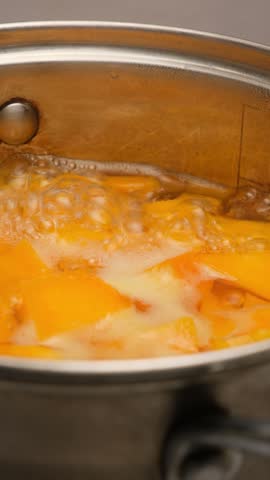 Orange pumpkin pieces boiling in hot water in pot. Cooking pumpkin for pumpkin puree soup. Vertical video. Pumpkin porridge. Orange pieces boiling in pot.