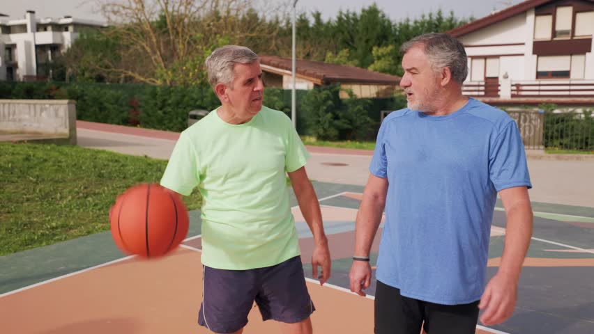 Two senior men enjoy their retirement playing basketball together on an outdoor court, embodying an active lifestyle and friendship through sport, promoting wellbeing and healthy aging