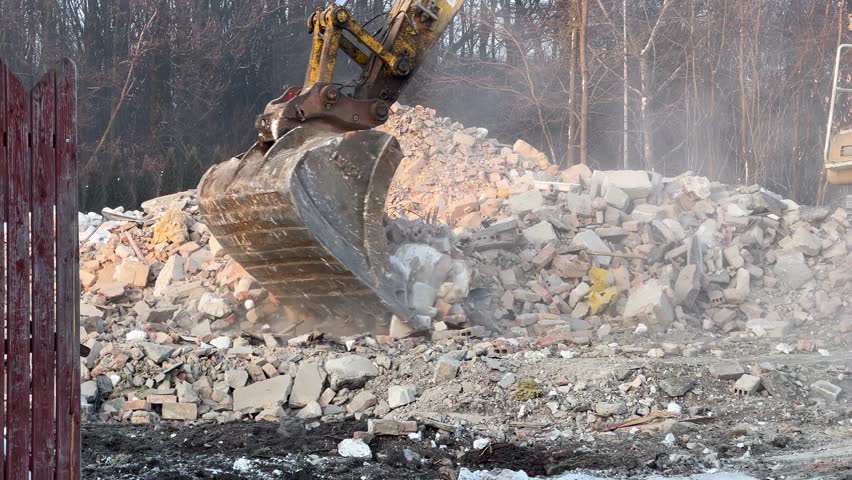 Heavy excavator clearing demolition waste, crushing bricks and concrete at a dusty construction site. Industrial machinery in action during site cleanup and redevelopment