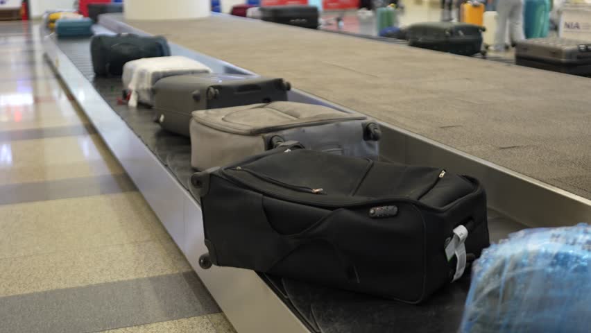 Suitcases moving on baggage conveyor belt at check-out area at arrival terminal in modern airport. Travel backpacks and suitcases moving around on luggage carousel in airport for passengers to pick up