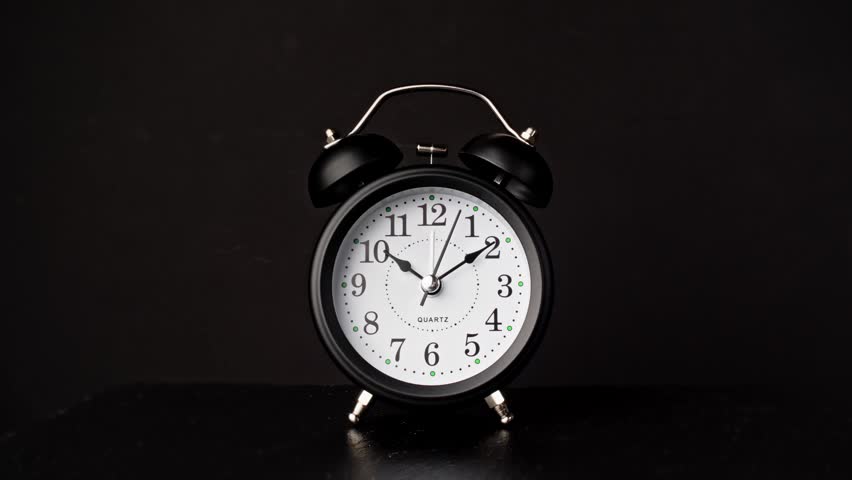 Black and white vintage alarm clock on black background. Old fashioned alarm clock with bells. Slider dolly shot. Time moving fast. Time concept. 4K, UHD