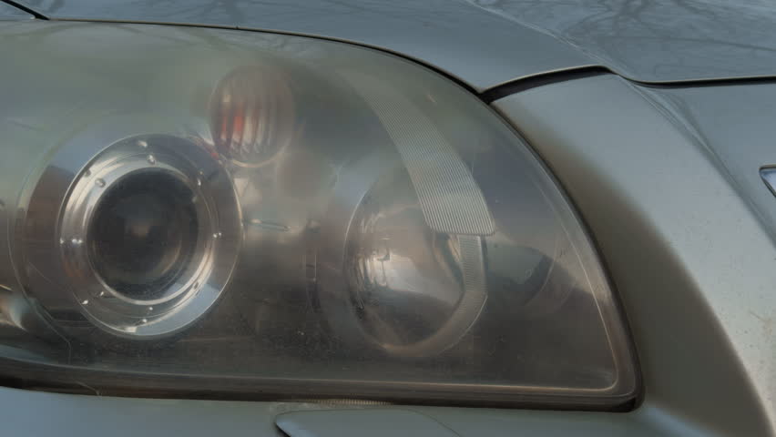 Reflections and scratches on lens. Closeup photograph emphasizing intricate details of car headlamp glass and chrome components
