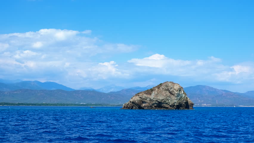 Sea stone against calm turquoise waves. View of turquoise sea waves by the rocks against clear sky in summer
