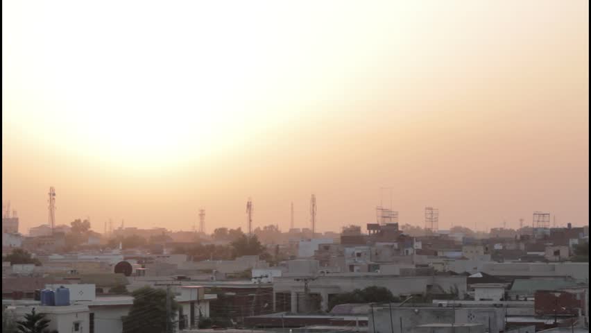 Time-lapse footage of Lahore, Pakistan during sunset, with the sun casting a warm orange glow across the horizon. Silhouettes of rooftops, communication towers, and urban buildings create a striking contrast against the colorful sky. The accelerated motion highlights the peaceful transition of light, blending natural beauty with the bustling urban landscape of Pakistan’s cultural capital.