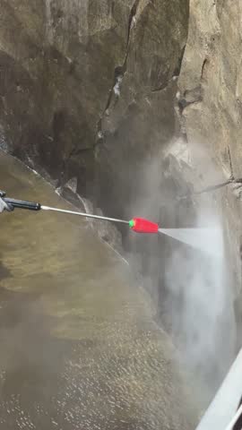 Worker cleaning stone wall with pressure washer removing dirt and algae in outdoor maintenance work. Worker cleans building exterior using a pressure washer.  Vertical video
