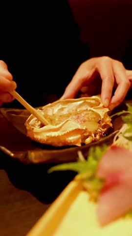Close-up shot of hands using a wooden spoon to scoop crab roe from a shell