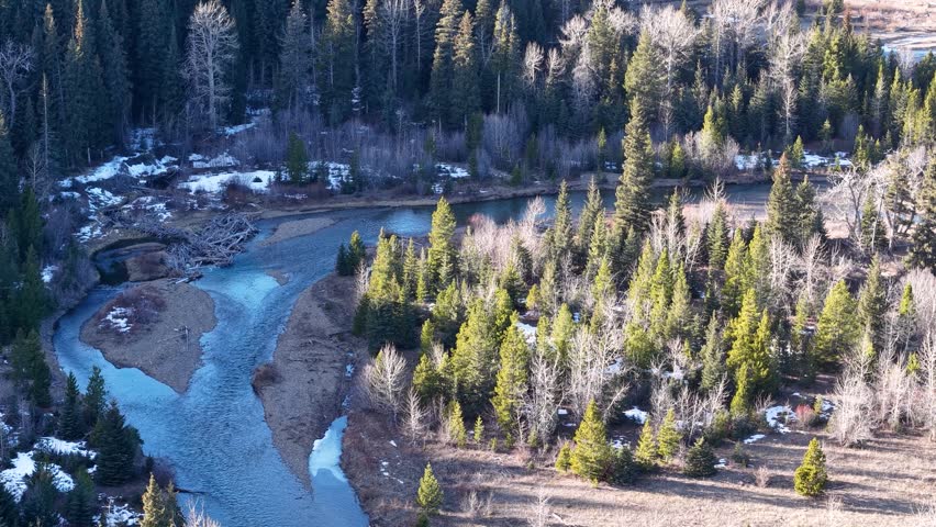 Aerial drone view of a winding turquoise river cutting through a rugged forested valley in Montana, with rocky banks and evergreen trees on both sides.