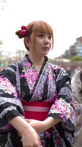 A young woman wearing a traditional floral yukata stands outdoors during a bright day
