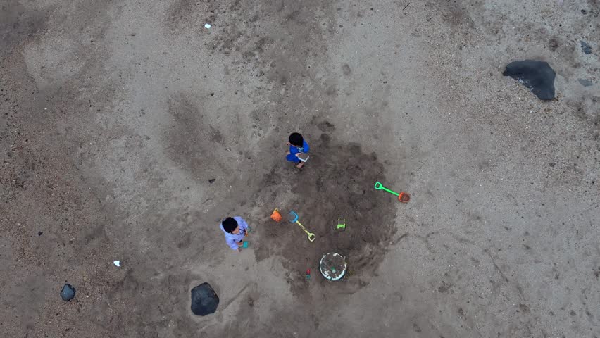 A high-angle view of two children playing on a rocky sandy beach.