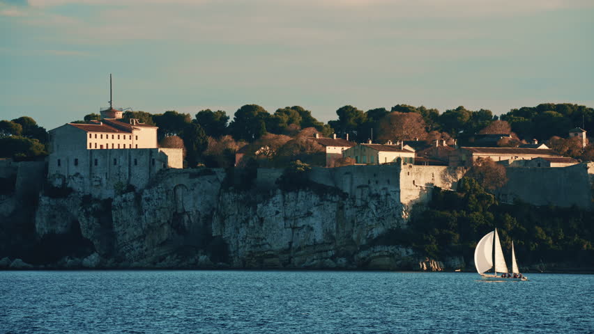 Sailboat floating on calm Mediterranean water in front of the historic Fort Carre in Antibes