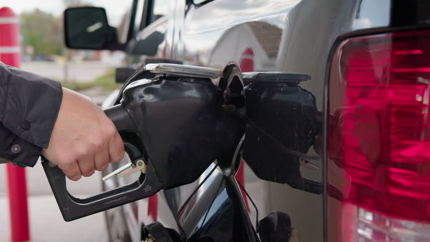 Driver refueling car at gas station and finishing fueling process reflecting.