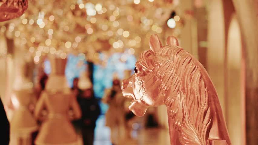 Elegant close-up of a decorative horse statue displayed inside a warmly lit hallway filled with golden holiday lights and ornaments