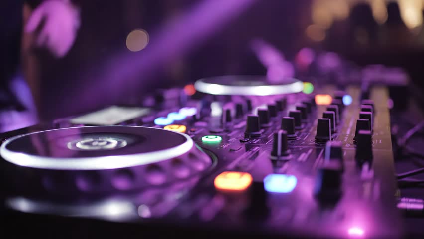 A close-up shot of a DJ mixer console with vibrant, colorful lights illuminating the buttons and turntables, creating an energetic atmosphere at a nightclub party.