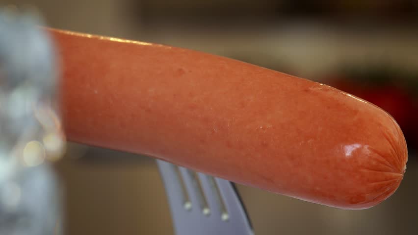 Close up of boiled sausage on fork is drizzled with tomato ketchup. Food. Meat